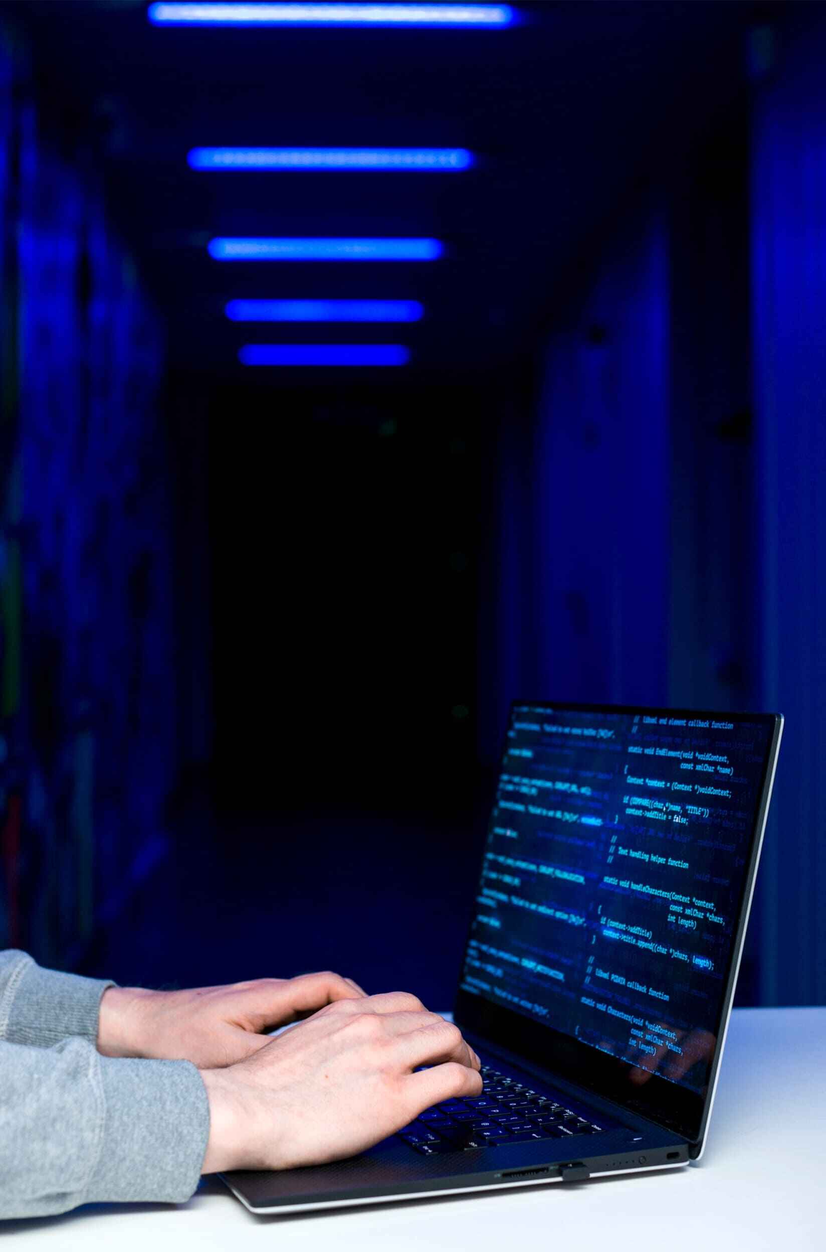 Hands typing on a laptop with blue neon lights, symbolizing coding and technology.